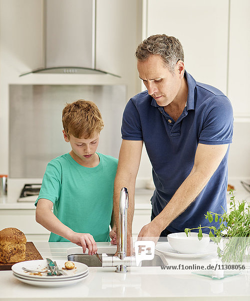 Ein Familienhaus. Ein Mann und ein kleiner Junge nebeneinander in der Küche beim Abwasch.