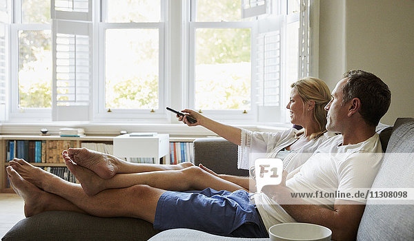 A couple  man and woman sitting on the sofa  watching television together  holding the remote control.