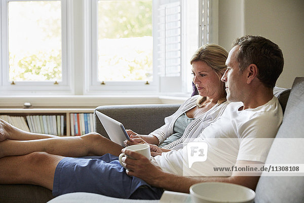 Ein Paar  das auf dem Sofa sitzt  eine Frau  die einen Laptop-Computer benutzt  und ein Mann  der in die Ferne schaut.