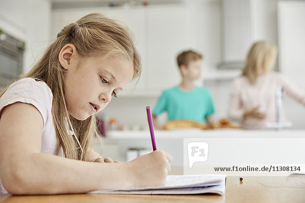 Ein Mädchen sitzt an einem Tisch in der Familienküche  hält einen Bleistift in der Hand und macht ihre Hausaufgaben.