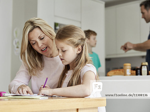 eine Frau und ihre Tochter  die an einem Tisch in der Küche sitzen und sich ihre Hausaufgaben ansehen.