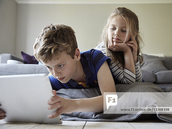 A family home. A boy and his sister looking at a digital tablet.