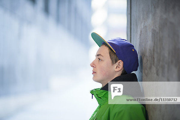 Teenage boy leaning against wall in city