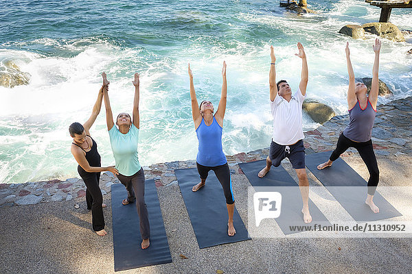 Instruktorin hilft Gruppe beim Yoga am Meer