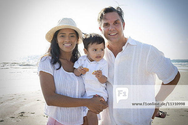 Porträt eines glücklichen Paares mit kleinem Sohn am Strand