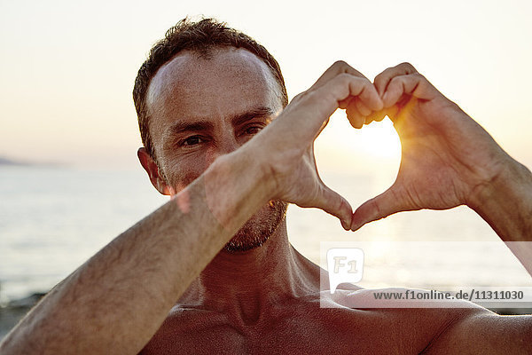 Porträt eines Mannes  der am Strand ein Herz formt