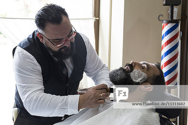 Barber putting shaving foam in man's beard