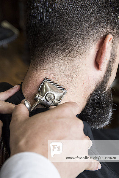 Friseur  der die Haare eines Mannes mit einer alten  handbetriebenen Haarschneidemaschine schneidet.