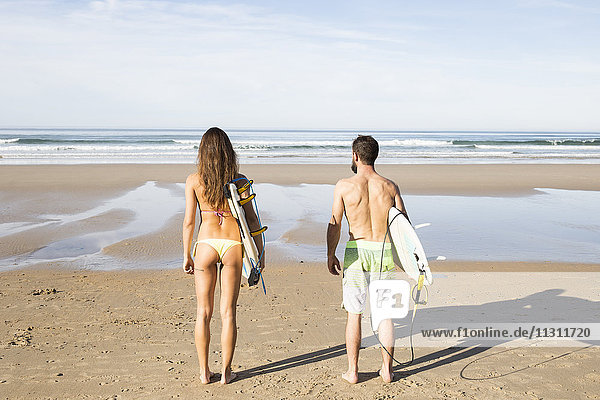 Couple carrying surfboards on the beach