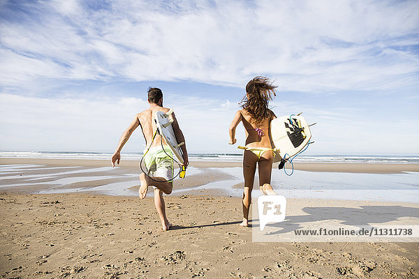 Couple carrying surfboards running on the beach