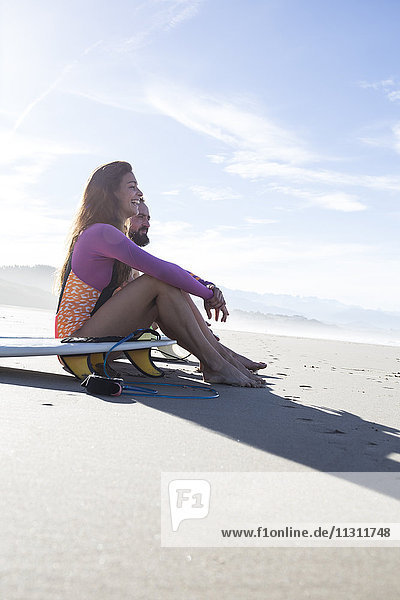 Couple with surfboards sitting on the beach