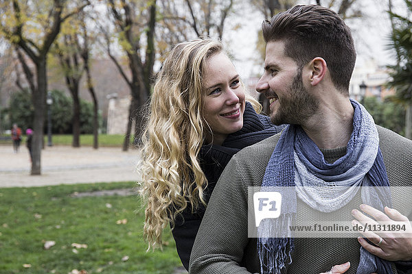 Ein Paar lächelt sich an und schaut sich in einem Park an.