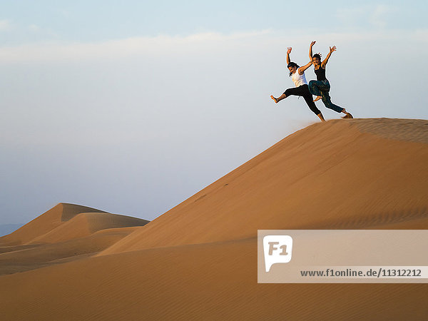 Oman  Al Raka  zwei junge Frauen  die von der Düne in der Wüste Rimal Al Wahiba springen.