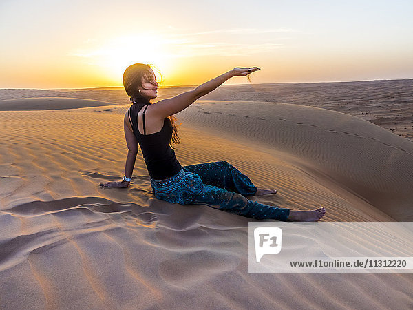 Oman  Al Raka  junge Frau sitzt auf einer Wüstendüne in der Wüste Rimal Al Wahiba.
