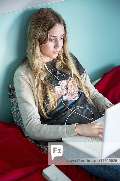 Junge Frau sitzt auf dem Bett und benutzt einen Laptop