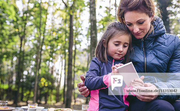 Mother and little daughter playing with smartphone in the woods