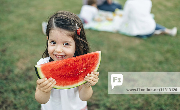 Portrait of smiling girl holding watermelon slice with her family in background