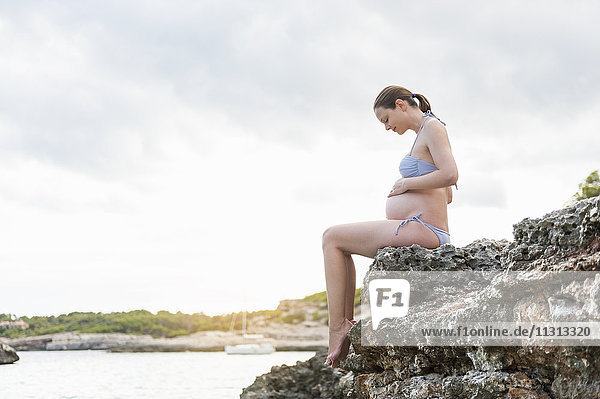 Schwangere Frau auf Felsen am Meer sitzend