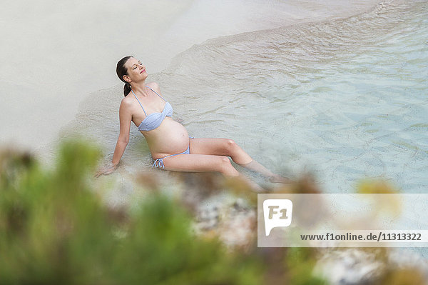 Schwangere Frau am Meer sitzend