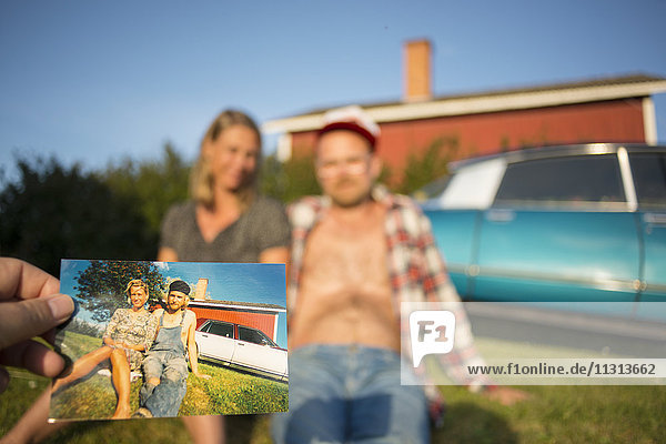 Menschen sitzen vor einem Haus mit einer Person  die ein Foto im Vordergrund hält