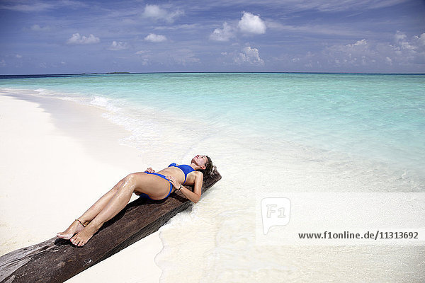 Malediven  Frau beim Sonnenbaden auf einem Baumstamm am Strand