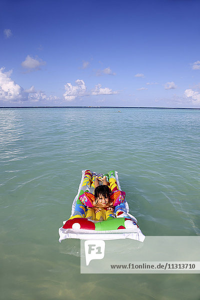 Malediven  Gulhi  Mädchen  das auf einem aufblasbaren Luftmatratzenbett im Wasser schwimmt.