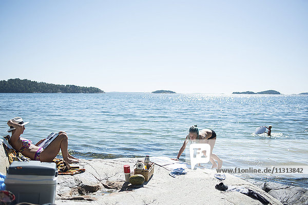 Frauen beim Sonnenbaden am See mit einem spielenden Jungen im Hintergrund