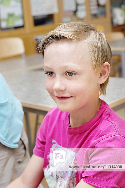 Junge mit blondem Haar sitzt im Klassenzimmer