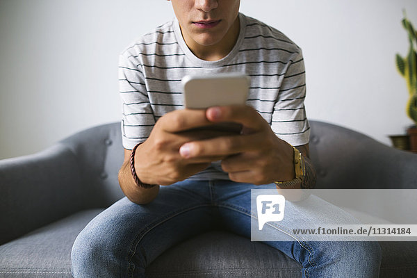 Teenager-Junge sitzt zu Hause auf der Couch und benutzt ein Handy.