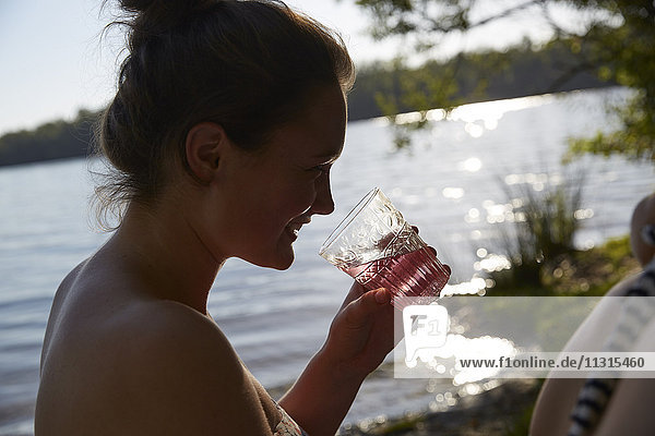 Lächelnde junge Frau am See bei einem Drink