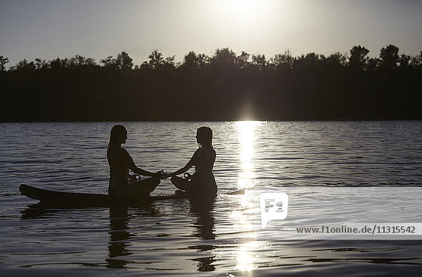 Two women doing yoga on paddleboard at sunset