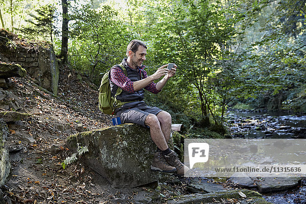 Wanderer im Wald auf Felsen an einem Bach sitzend  mit Selbstbedienung