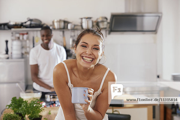 Porträt der lachenden jungen Frau mit Kaffeetasse in der Küche