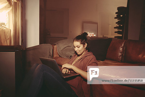 Young woman relaxing with laptop in the lighted living room