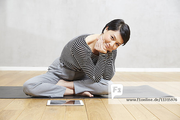 Lächelnde Frau sitzend auf Yogamatte mit Tablette