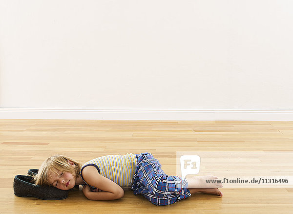 Kleiner Junge auf Holzboden liegend mit Kopf auf Hausschuhen