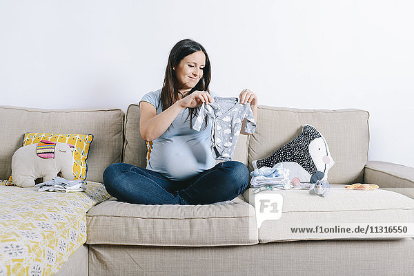 Schwangere Frau sitzt auf der Couch und schaut auf Babyschläfer.