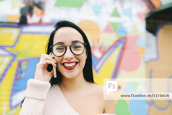 Porträt einer glücklichen Frau am Telefon vor der Graffiti-Wand