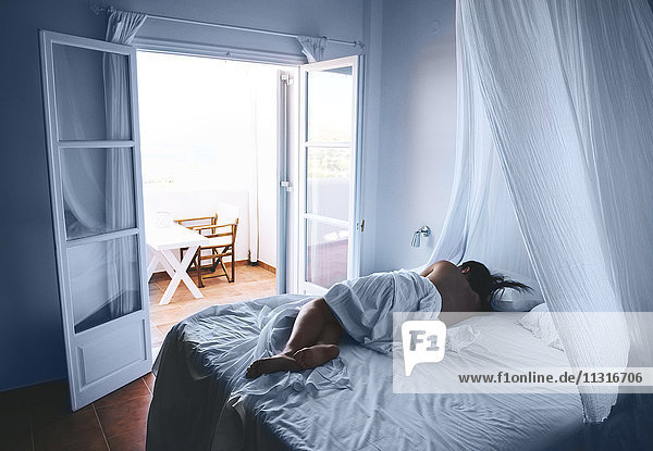 Greece  Milos  Woman sleeping in white sheets with open balcony door