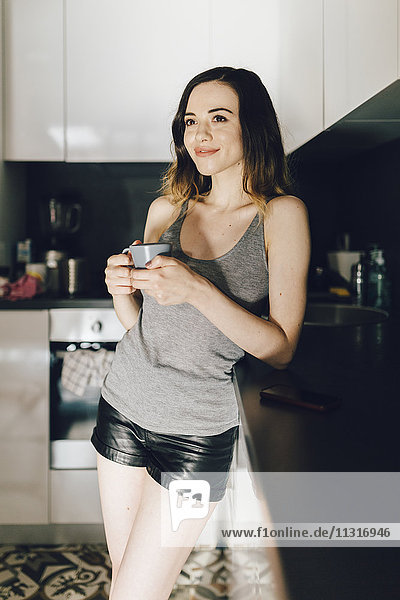 Smiling young woman drinking coffee in kitchen