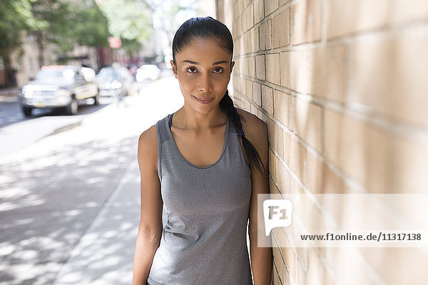 Portrait of confident female athlete leaning against brick wall