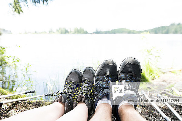 Die Beine eines Paares auf einer Wanderung,  die am See ruht