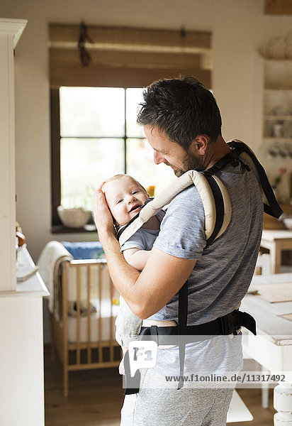 Happy father with baby in baby carrier at home