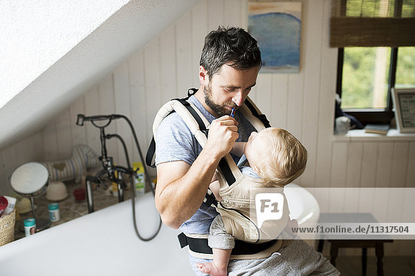 Father with baby in baby carrier brushing his teeth