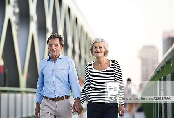 Seniorenpaar  das Hand in Hand auf einer Brücke geht.