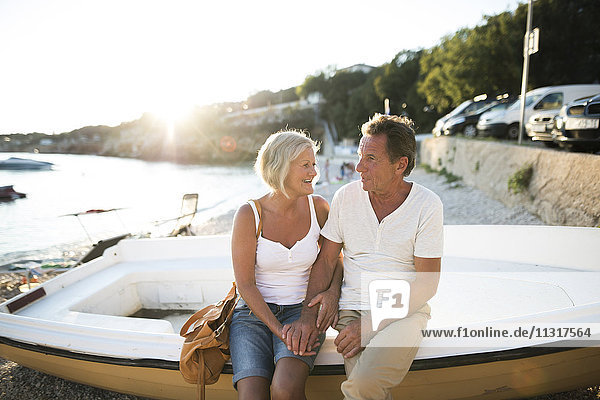 Senior couple sitting on edge of a boat on the beach at evening twilight