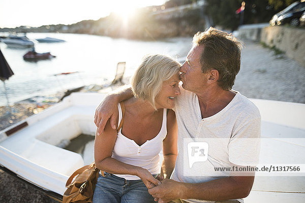 Senior couple sitting on edge of a boat on the beach at evening twilight