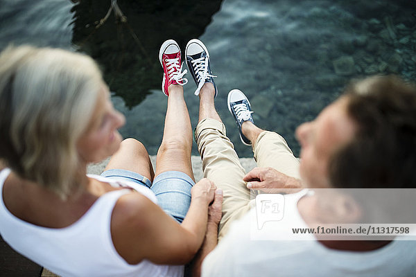Senior couple sitting on jetty wearing sneakers