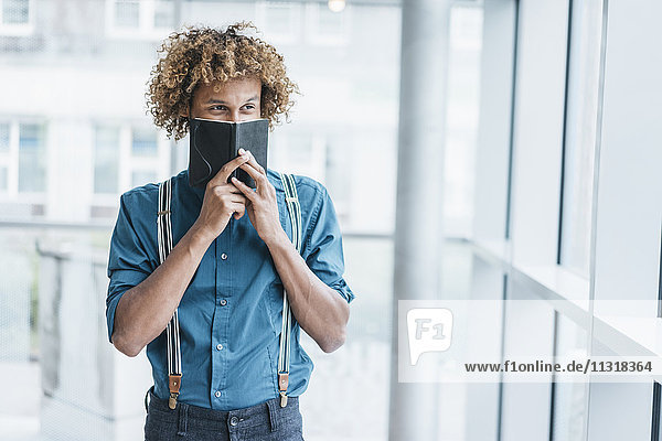 Junger Mann bedeckt Gesicht mit Notizbuch
