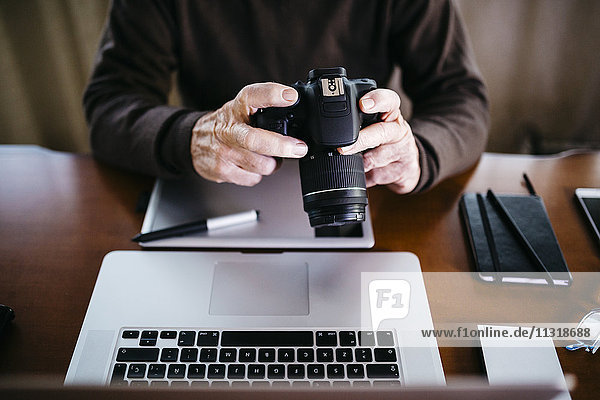 Senior Fotograf mit Laptop und Digitalkamera zu Hause  Teilansicht